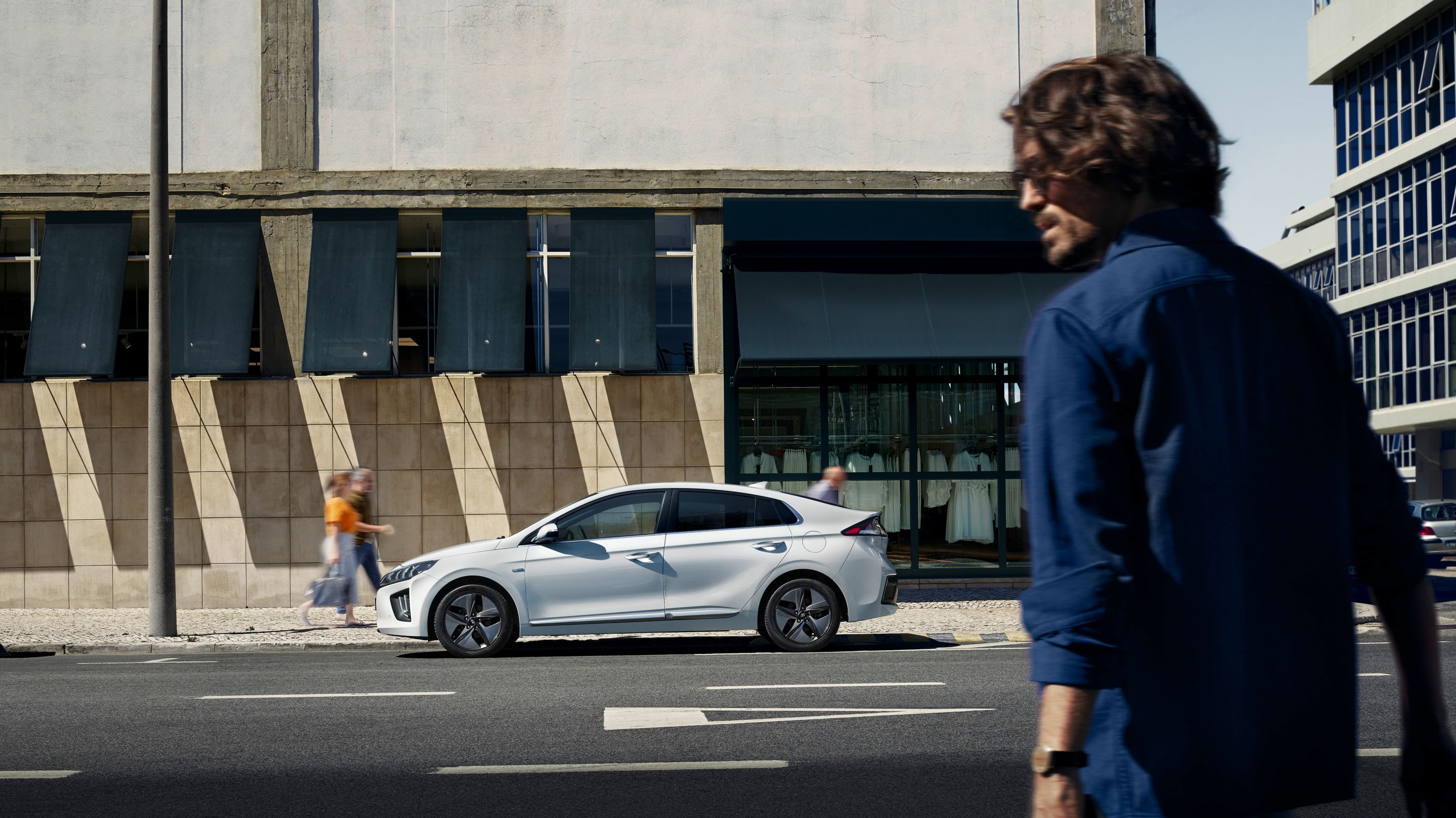 Muž, chytající se přejít silnici, aby se dostal ke svému zaparkovanému Hyundai IONIQ. V ruce drží chytrý telefon.